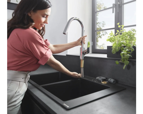 Femme installant un robinet de cuisine chromé dans un évier noir.