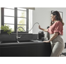 Cuisine moderne avec double évier, robinet et machine à café, une femme remplit la machine à café d''eau.