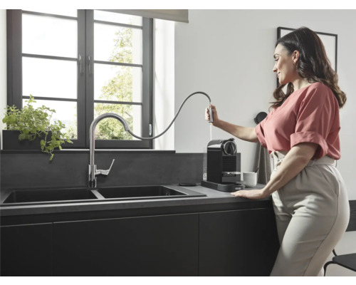 Cuisine moderne avec double évier, robinet et machine à café, une femme remplit la machine à café d''eau.