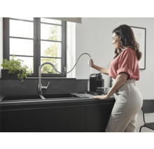 Une femme remplit le réservoir d''eau d''une machine à café noire à côté d''un évier dans une cuisine moderne.