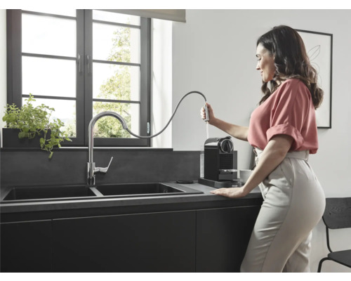 Une femme remplit le réservoir d''eau d''une machine à café noire à côté d''un évier dans une cuisine moderne.