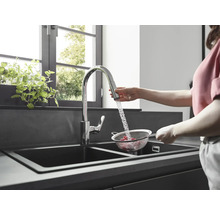 Une femme lave des framboises dans une passoire sous un robinet dans une cuisine moderne avec un évier double