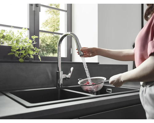 Une femme lave des framboises dans une passoire sous un robinet dans une cuisine moderne avec un évier double