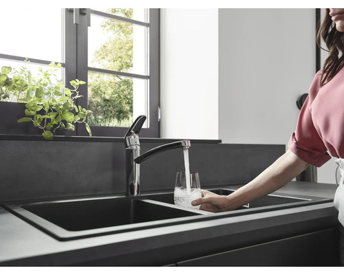 Scène de cuisine avec évier double, robinet et personne remplissant un verre d''eau