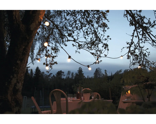 Table de jardin illuminée avec guirlande lumineuse sur les branches d''arbres pour une ambiance chaleureuse