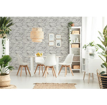 Salle à manger lumineuse avec table, chaises, étagère et éléments décoratifs devant un mur avec du papier peint imitation pierre.
