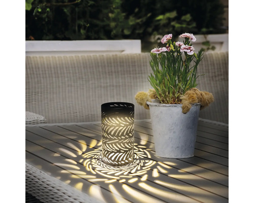 Dekorative Tischleuchte mit Blattmuster neben einem Blumentopf auf einem Gartentisch