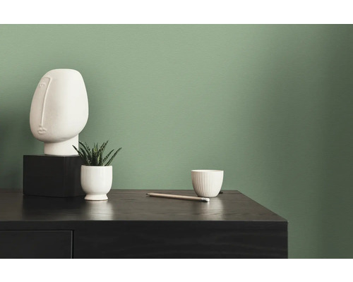 Dekorative weiße Skulptur, Zimmerpflanze und Schale auf einer schwarzen Kommode vor einer grünen Wand