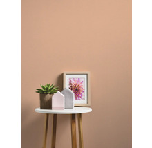 Dekorative Szene mit Zimmerpflanze, Hausmodellen und gerahmtem Blumenbild auf einem Beistelltisch vor einer farbigen Wand