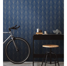 Raumansicht mit blau gemusterter Tapete, Schreibtisch, Fahrrad und Hocker