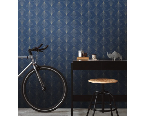 Raumansicht mit blau gemusterter Tapete, Schreibtisch, Fahrrad und Hocker