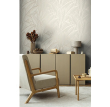 Wohnzimmer mit beiger Blättertapete, Sessel und Sideboard.