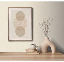 Arrangement décoratif avec une image encadrée avec un motif circulaire abstrait, un vase avec des fleurs séchées, une tasse et des livres sur une table.