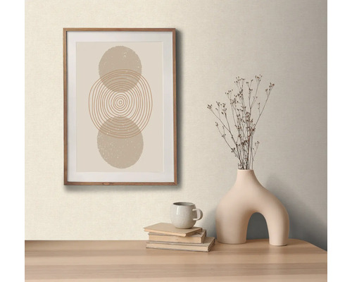 Arrangement décoratif avec une image encadrée avec un motif circulaire abstrait, un vase avec des fleurs séchées, une tasse et des livres sur une table.