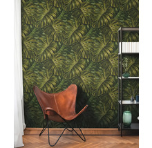 Pièce avec papier peint à feuilles de Monstera, fauteuil en cuir et bibliothèque