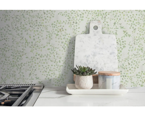 Mur décoratif à motif de feuilles, planche à découper, plante en pot et récipient sur une table de cuisine.