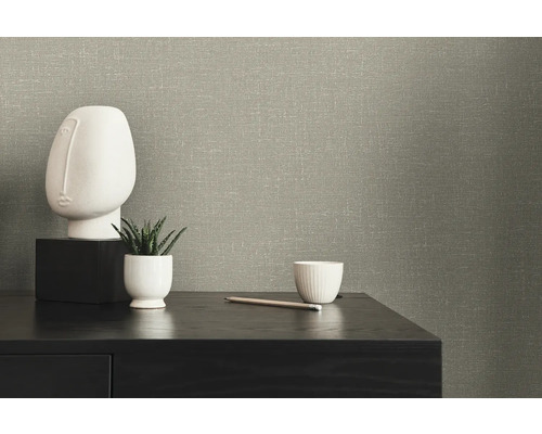 Nahaufnahme einer Wand mit strukturierten Tapeten, einem dekorativen Gesicht, einer Sukkulente und einer Tasse auf einem Tisch.