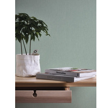 Dekoratives Arrangement mit Pflanze in Papierverpackung und Büchern auf einem Holztisch vor einer Wand