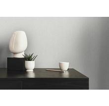 Nahaufnahme einer strukturierten Tapete mit minimalistischer Dekoration auf einer dunklen Holzkommode.