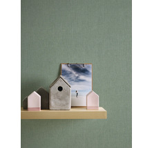 Dekorative Szene mit Holzregal, Zierhäusern und Klemmbrett vor einer grünen Wand