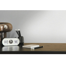 Dekoratives Zimmer mit Uhr, Stiften, Notizblock und Lampe auf einem dunklen Holztisch vor einer einfarbigen Wand.