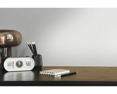 Dekoratives Zimmer mit Uhr, Stiften, Notizblock und Lampe auf einem dunklen Holztisch vor einer einfarbigen Wand.