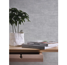 Nahaufnahme einer Wand mit Mustertapete, einem Holztisch, einer Zimmerpflanze und Büchern.