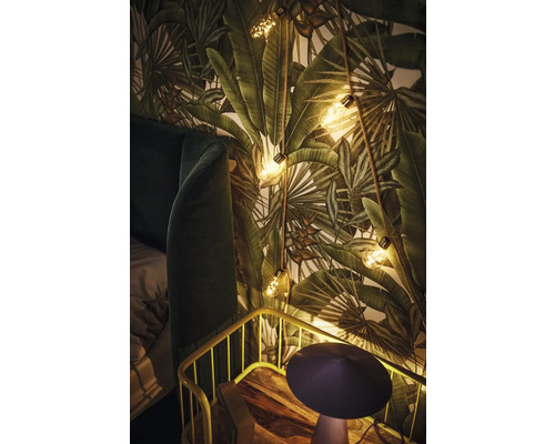 Dekoratives Schlafzimmer mit Pflanzenmustertapete, Lichterkette und Nachttisch.