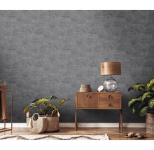 Wohnzimmer mit grauer Strukturtapete, Holzkommode, Tischlampe und Zimmerpflanzen.