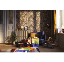 Wohnzimmer mit gemusterter Tapete, blauem Sessel und Strickdecke