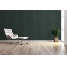 Wohnraum mit grüner Blättertapete, Sessel, Fusshocker, Topfpflanze und Holzboden