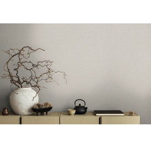 Gros plan d''une commode décorée avec vase, branches et théière devant un papier peint beige.