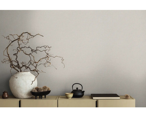 Gros plan d''une commode décorée avec vase, branches et théière devant un papier peint beige.