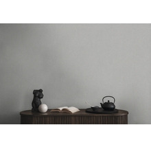 Nature morte décorative avec théière, livre et sculpture sur une armoire en bois devant un mur uni.