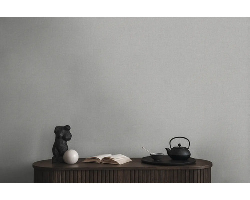 Nature morte décorative avec théière, livre et sculpture sur une armoire en bois devant un mur uni.