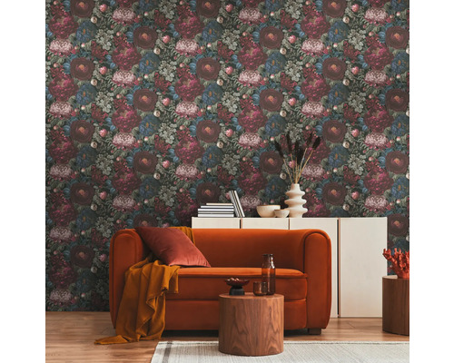 Salon avec papier peint à motif floral, canapé orange et tables en bois sur un tapis