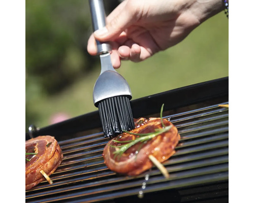 Une personne badigeonne de la viande avec un pinceau sur un gril.