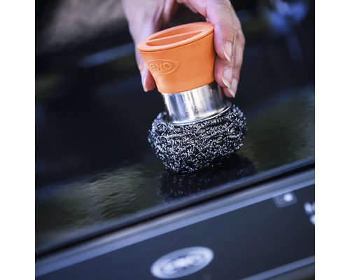 Une main tient un tampon à récurer avec une poignée sur une surface.