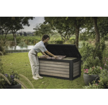 Eine Frau räumt eine Gartenbox im Garten ein. Die Gartenbox ist aus Holz und Kunststoff.