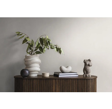 Dekorative Gegenstände auf einem Holzschrank: eine Vase mit Pflanzen, eine runde Dose, Bücher mit einer herzförmigen Figur und eine Frauenstatuette.