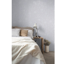 Schlafzimmer mit Bett, Nachttisch, Lampe und Tapete mit Pflanzenmuster