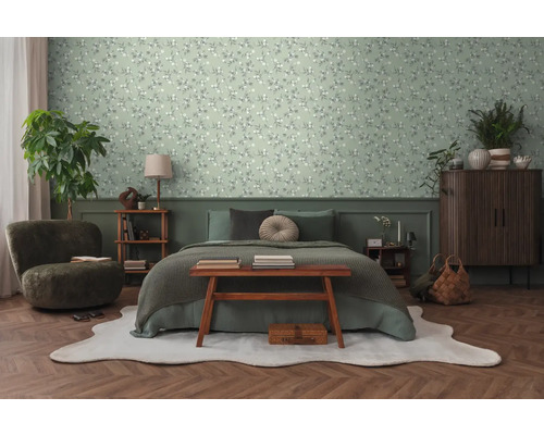 Schlafzimmer mit Bett, Sessel, Kommode und floraler Tapete.