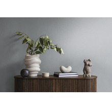 Dekorative Anordnung auf einem Holzschrank mit Vase, Grünpflanzen, Büchern und Skulpturen.