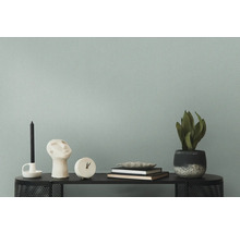 Dekorative Szene auf einem schwarzen Regal mit Kerze, Skulptur, Uhr, Büchern und einer Topfpflanze vor einer Wand.