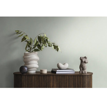 Dekoratives Interieur mit Vase, Pflanzen, Büchern und Skulptur auf einer Kommode.