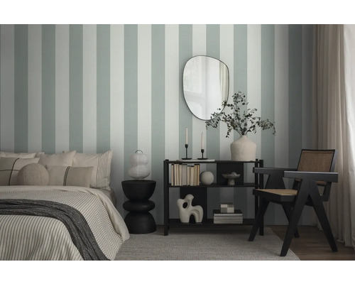 Schlafzimmer mit Bett, Beistelltisch, Regal und Stuhl vor einer gestreiften Wandtapete