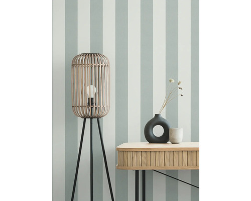 Raumansicht mit Holzstehlampe, Tisch und Dekoration vor gestreifter Wand