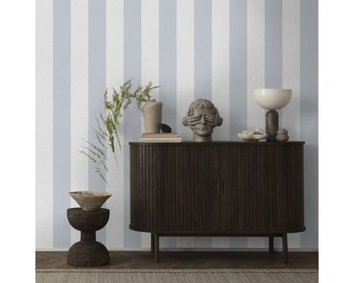 Wohnraum mit gestreifter Tapete, Kommode und Dekorationen.