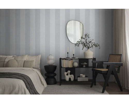 Schlafzimmer mit Bett, Kommode, Spiegel und Stuhl vor gestreifter Tapete.