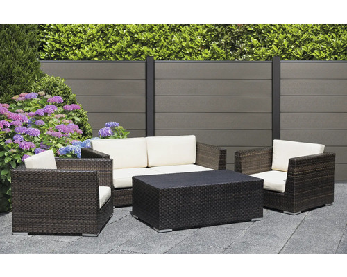 Gartenlounge-Set mit Sofa, Sesseln und Tisch auf einer Terrasse vor einem Zaun und Pflanzen